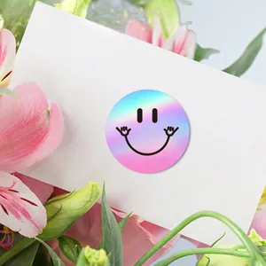 Close-up detail of a holographic laser smiley sticker on a white card with pink floral background