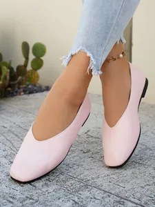Close-up of pink square-toe leather flat shoes worn with blue jeans and an anklet.
