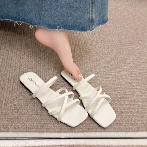 Dettaglio di sandali piatti bianchi con sottili cinturini incrociati e punta quadrata alla moda.