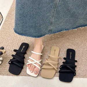 Eleganti sandali piatti a punta quadrata in nero, bianco e beige su un tappeto intrecciato