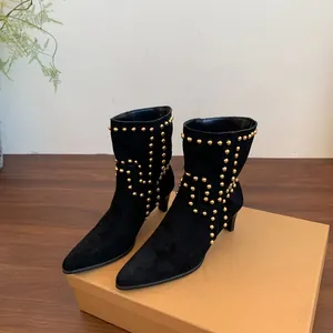 Detalle de botines de ante negro con tachuelas doradas y tacón de aguja bajo.