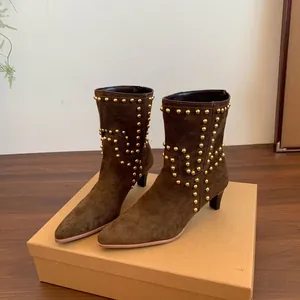 Detalle de elegantes botines de ante marrón con tachuelas doradas y diseño de punta afilada.