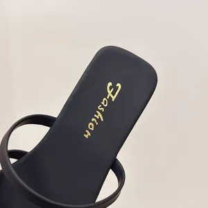 Primo piano di sandali piatti neri a punta quadrata con elegante logo Fashion oro.