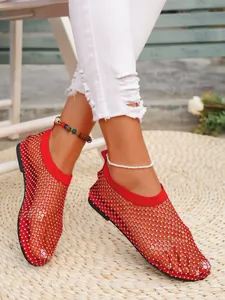 Primo piano di sandali bassi a rete rossi da donna con decorazioni di strass brillanti.