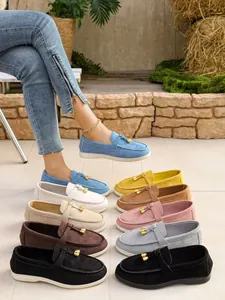 Assorted colors of women's suede loafers with gold buckles on an outdoor stone floor