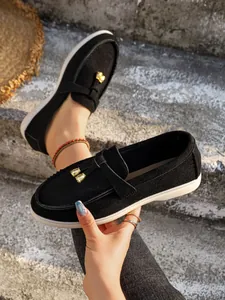 Close-up of women's black suede slip-on loafers with gold bell charms and white soles.