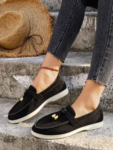 Close-up detail of stylish black suede loafers featuring decorative gold-tone bell tassels