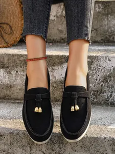 Detail view of black suede loafers with gold tassels and white platforms on stone steps.