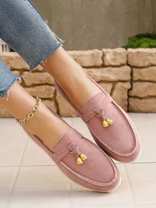 Close-up of pink suede loafers with elegant gold tassel charms and white stitching.