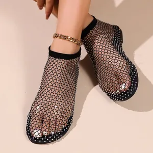 Vista dettagliata di sandali bassi neri in rete con strass indossati da una modella.