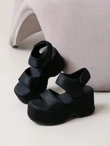 Gros plan sur des sandales compensées noires avec brides velcro réglables et fini mat.
