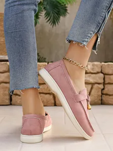 Close-up detail view of pink suede slip-on loafers featuring a stylish gold charm pendant