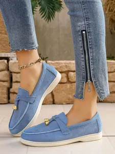 Detail of light blue denim loafers for women with golden bell charms on model