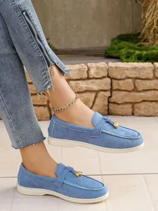 Detailed macro view of stylish blue textured slip-on loafers with gold buckle ornament on feet.