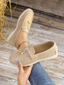 Beige suede slip-on loafers for women with gold charm details in a rustic setting
