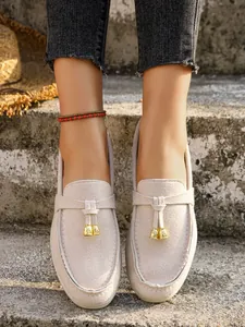 Close-up of women's beige suede loafers with gold bell decorative tassels on concrete