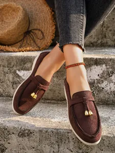 Close-up detail of brown suede slip-on loafers with elegant gold tassel charms on stone steps