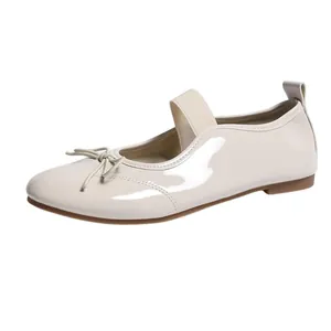 Close-up of beige patent leather Mary Jane flats with bow detail and elastic strap