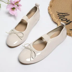 Detailed view of cream patent leather ballet flats with elastic strap and bow
