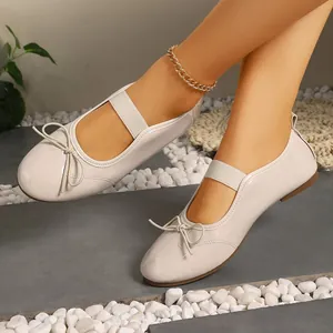 Close-up of beige patent leather Mary Jane flats featuring a bow and elastic strap