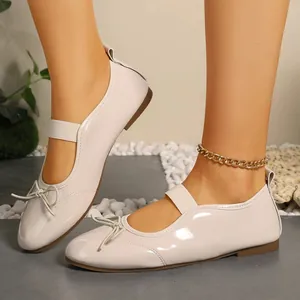 Detailed view of elegant cream patent leather ballet flats with bow and strap on feet