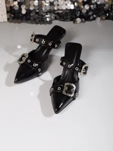 Detailansicht von schwarzen Lackleder-High-Heels mit Strassschnallen und Ösenriemen.