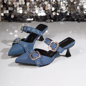 Detailansicht stilvoller blauer Denim-Mules mit spitzer Kappe, Strassschnallen und Pfennigabsatz.