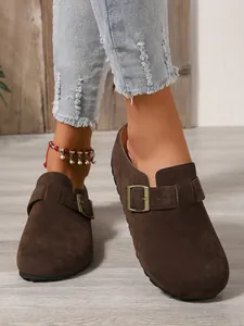 Close-up detail of brown suede slip-on clogs featuring an adjustable buckle strap