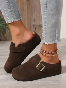 Macro view of stylish brown suede slip-on clogs with metal buckle worn by a model.