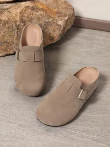 Detail view of women's khaki suede clogs with an adjustable buckle strap on wood.
