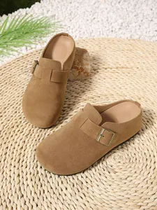 Close-up detail of women's camel suede clogs with buckle strap on a natural woven mat