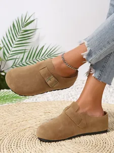 Detailed view of women's casual tan suede clogs with buckle strap on a woven mat