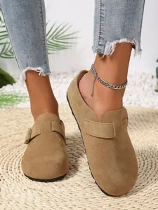 Detailed view of camel suede clogs featuring a metal buckle strap on a straw mat