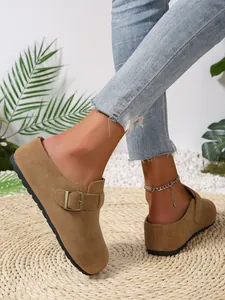 Close-up of tan suede buckle mules worn on a woven straw mat outdoors