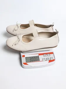 Detail view of beige patent leather flat shoes being weighed on a digital scale