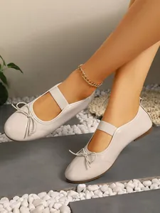 Elegant beige patent leather Mary Jane flats with bow and elastic strap detail view