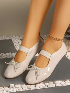 Detailed close-up view of beige patent leather ballet flats with bow and elastic strap