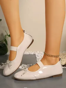 Detailed view of off-white glossy patent leather Mary Jane flats with elastic strap and bow