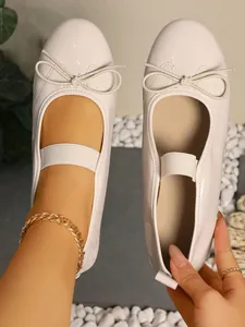 Close-up view of cream patent leather Mary Jane ballet flats with bow and strap