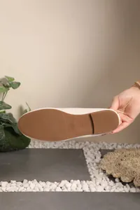 Detailed view of the textured brown rubber sole on a beige women's flat shoe