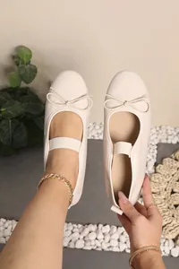 Close-up view of cream patent leather ballet flats with bow detail and elastic strap