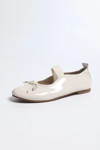 Detailed side view of cream patent leather ballet flats with bow and elastic strap detail