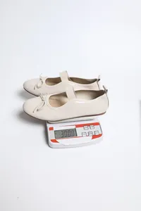 Close-up of beige patent leather Mary Jane flats being weighed on a digital scale
