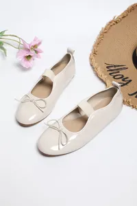Elegant cream patent leather flats with bow detail and elastic strap on a white surface