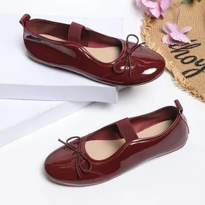 Wine red patent leather ballet flats with bow detail and elastic strap on a white stand