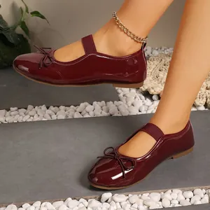 Detail view of burgundy patent leather Mary Jane flats featuring a bow and elastic strap