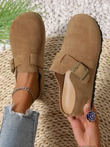 Close-up detail of casual brown suede buckle clogs worn with denim on straw mat