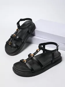 Dettaglio di sandali piatti neri minimalisti con eleganti borchie circolari dorate lucide