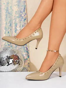 Detailansicht von beigen Stilettos mit spitzen Zehen und goldenen Nietendetails am Modell.