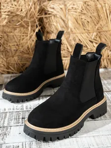Close-up of black suede Chelsea boots with chunky lug soles and tan stitching.